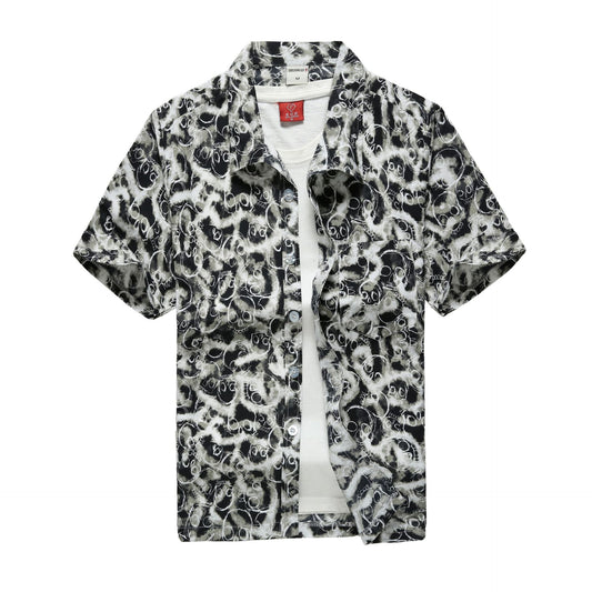 Tropical button-up shirt featuring a black base with green palm leaves, red hibiscus flowers, and airplane motifs, displayed flat to showcase summer-ready, relaxed styling.