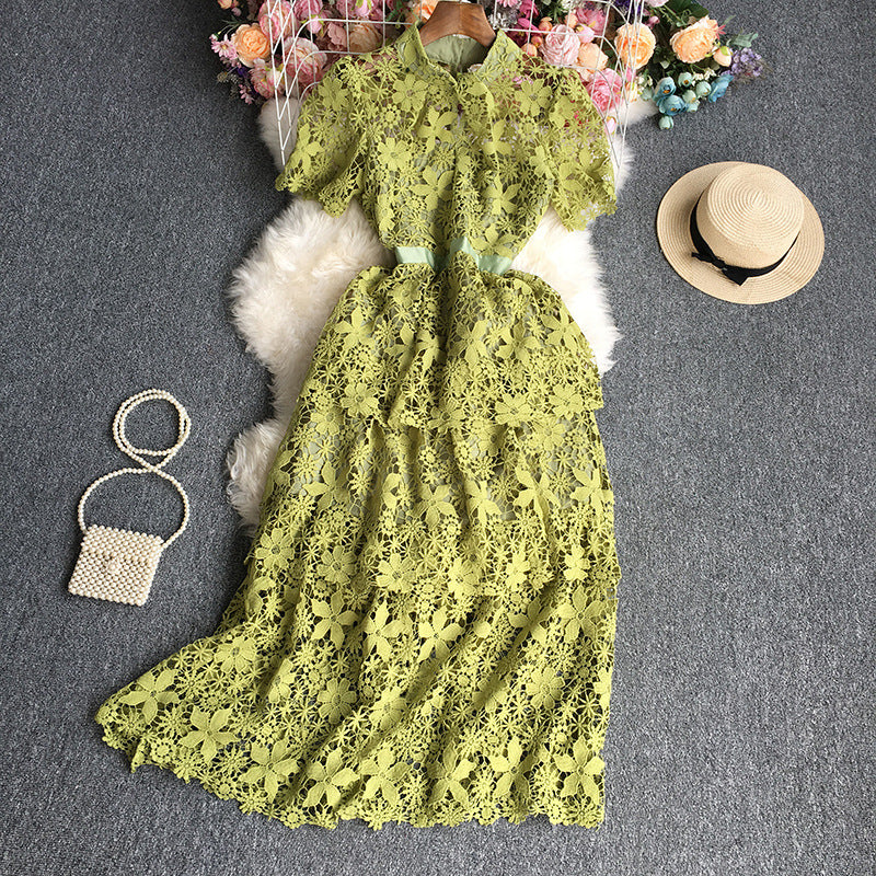 Green lace dress on a gray surface with a hat and handbag nearby