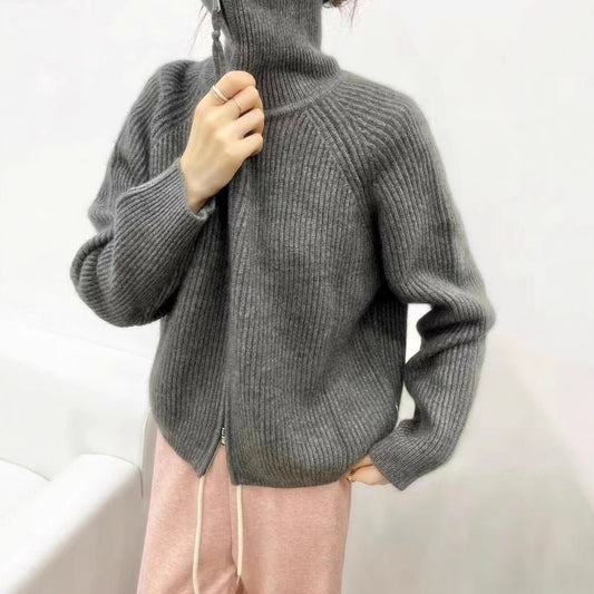 Woman wearing a grey ribbed knit sweater with a high collar and a partially zipped front, styled with light pink pants and delicate accessories—cozy, stylish, and perfect for layering
