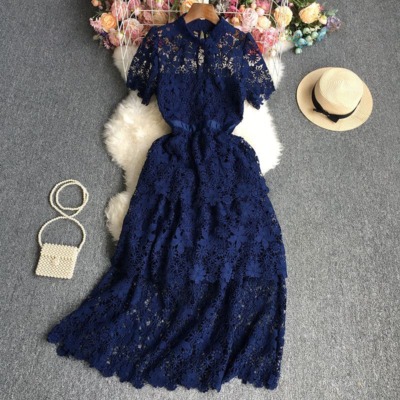 Navy blue lace dress on a gray surface with a straw hat and small bag.