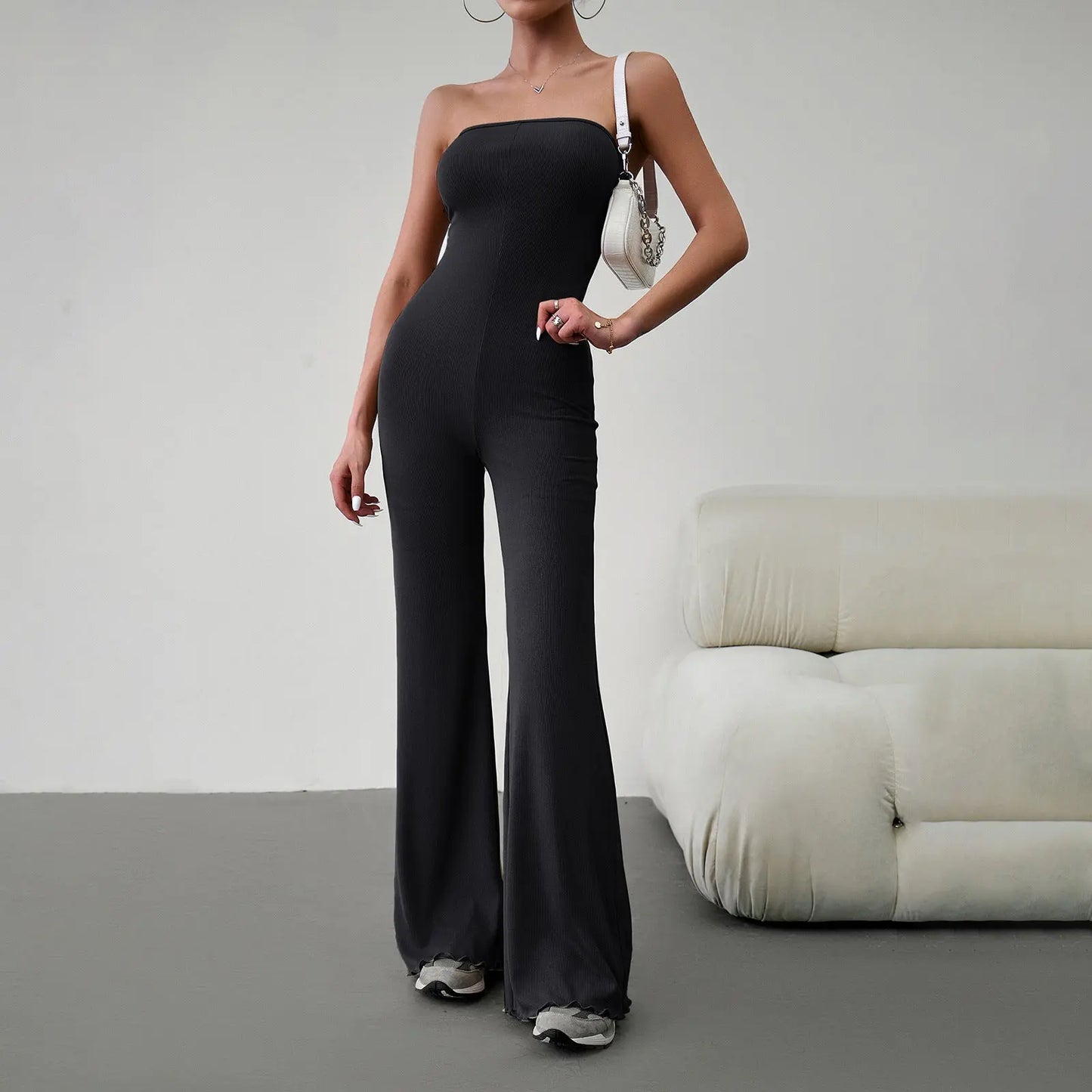 Elegant strapless jumpsuit available in beige, blue, brown, light beige, and black – form-fitting with a flared bottom, paired with sneakers and a white handbag.
