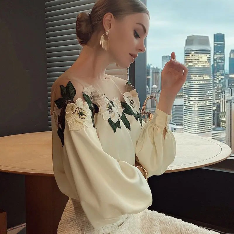 Woman wearing an off-the-shoulder blouse with white floral embroidery and puffed sleeves, paired with a textured high-waist skirt—sophisticated, chic, and perfect for both casual and dressy outfits.