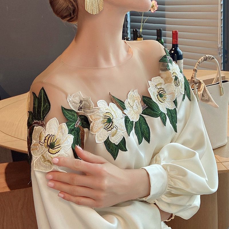 Woman wearing an off-the-shoulder blouse with white floral embroidery and puffed sleeves, paired with a textured high-waist skirt—sophisticated, chic, and perfect for both casual and dressy outfits.