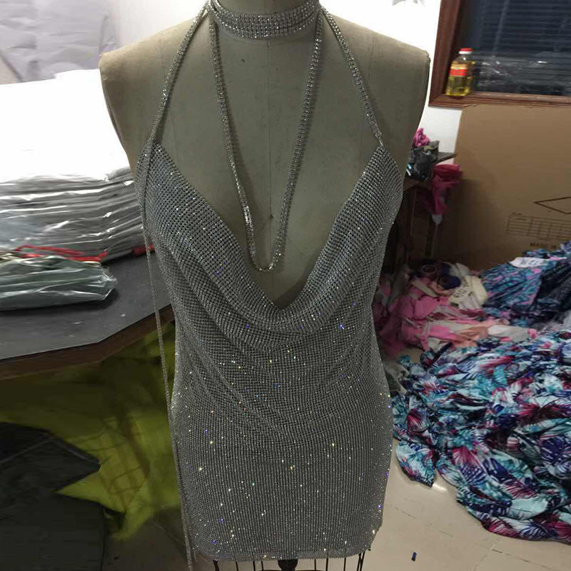 Front view of a metallic halter-neck gown with open back and thigh-high slit, shown in both silver and gold versions, styled in a formal dining setting with soft lighting
