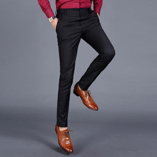 Multiple views of structured tailored trousers in navy, grey, black, and additional colours, styled with a white shirt and brown shoes, highlighting pleats, tapered legs, and buttoned back pockets
