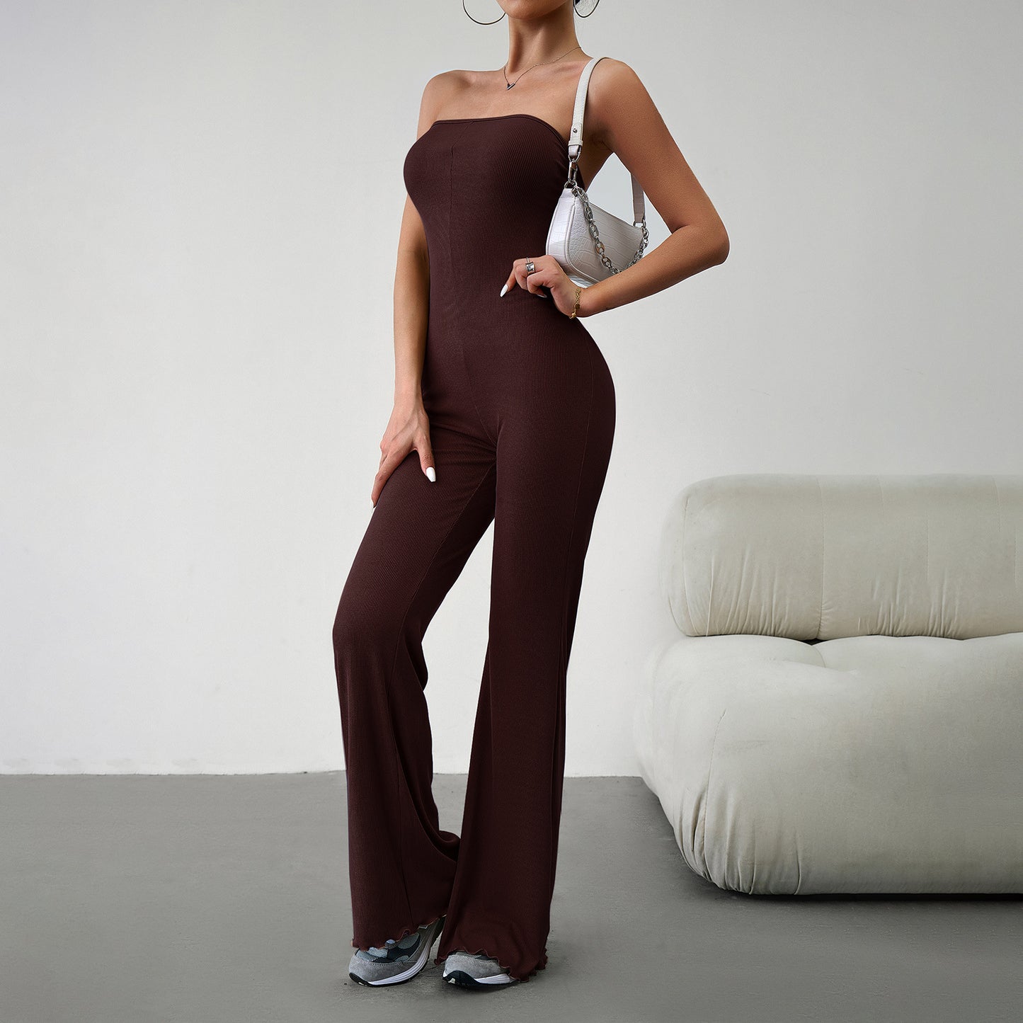 Elegant strapless jumpsuit available in beige, blue, brown, light beige, and black – form-fitting with a flared bottom, paired with sneakers and a white handbag.