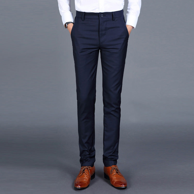 Multiple views of structured tailored trousers in navy, grey, black, and additional colours, styled with a white shirt and brown shoes, highlighting pleats, tapered legs, and buttoned back pockets