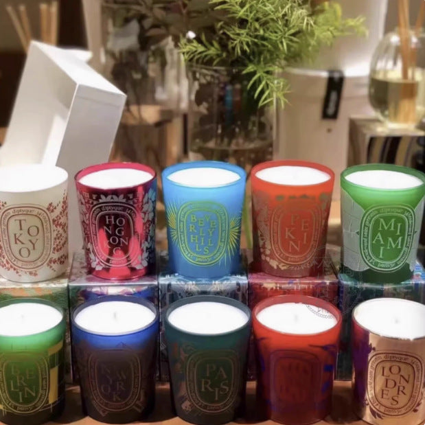 Display of Diptyque candles in clear glass jars with white labels, showcasing 24 visible scents including Baies, Tubereuse, Patchouli, and Gardenia, arranged in rows with varied wax colours