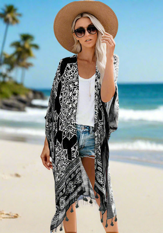 Woman wearing a patterned boho kimono-style cover-up in blue, paired with a wide-brimmed hat, white top, and denim shorts. Smaller images feature the same cover-up in black, teal, and rust colors—elegant, flowy, and perfect for layering.