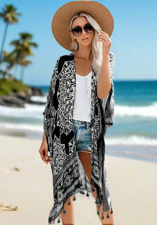 Woman wearing a patterned boho kimono-style cover-up in blue, paired with a wide-brimmed hat, white top, and denim shorts. Smaller images feature the same cover-up in black, teal, and rust colors—elegant, flowy, and perfect for layering.