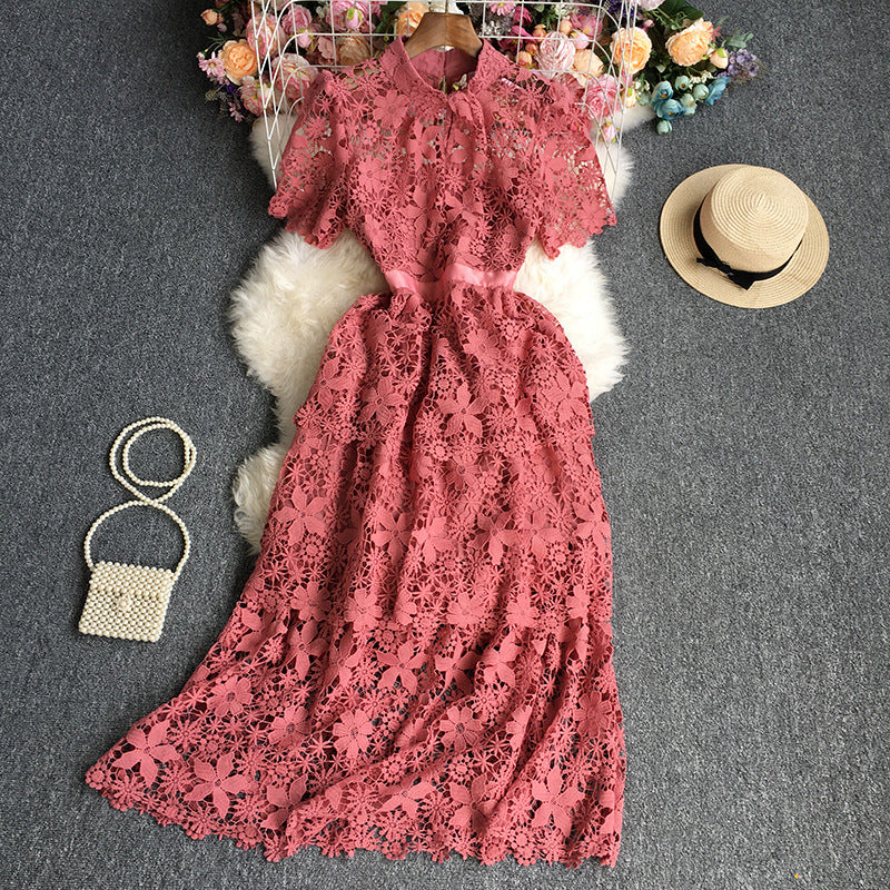 Pink lace dress on a dark surface with a straw hat and handbag nearby.