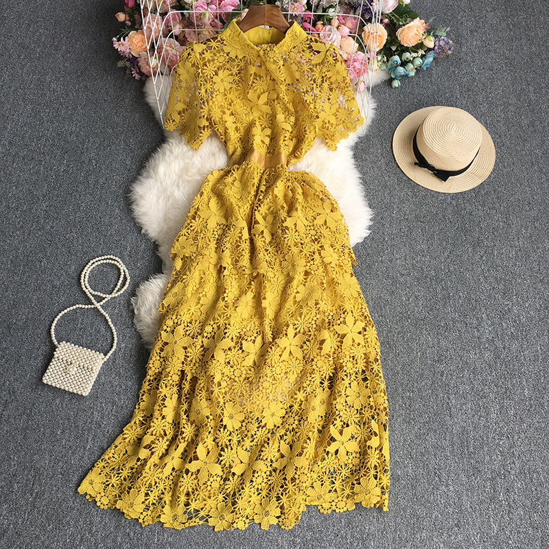 Yellow lace dress on a gray surface with a straw hat and small bag nearby.