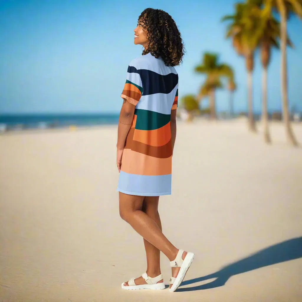 Person wearing a colorful striped t-shirt dress with shades of blue, orange, green, and brown, paired with white sandals, standing on a paved pathway lined with palm trees—stylish, vibrant, and perfect for sunny days.