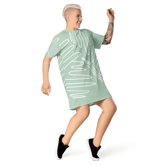Light green oversized t-shirt dress featuring white abstract line patterns, worn with black sneakers—modern, artistic, and perfect for casual street-style fashion.