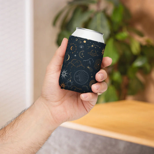Hand holding a black can cooler with celestial-themed prints in gold and white—featuring stars, planets, clouds, and an eye, wrapped around a slim can—stylish, insulated, and available in two sizes.