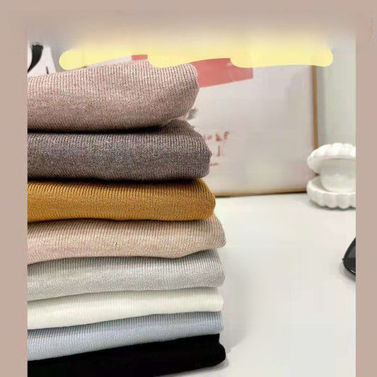 Woman wearing a ribbed light-colored turtleneck sweater, accessorized with hoop earrings, a delicate necklace, and rings—cozy, elegant, and perfect for chilly days.