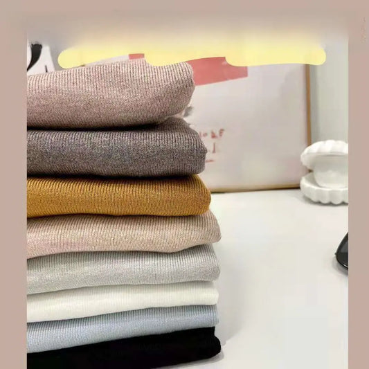 Woman wearing a ribbed light-colored turtleneck sweater, accessorized with hoop earrings, a delicate necklace, and rings—cozy, elegant, and perfect for chilly days.