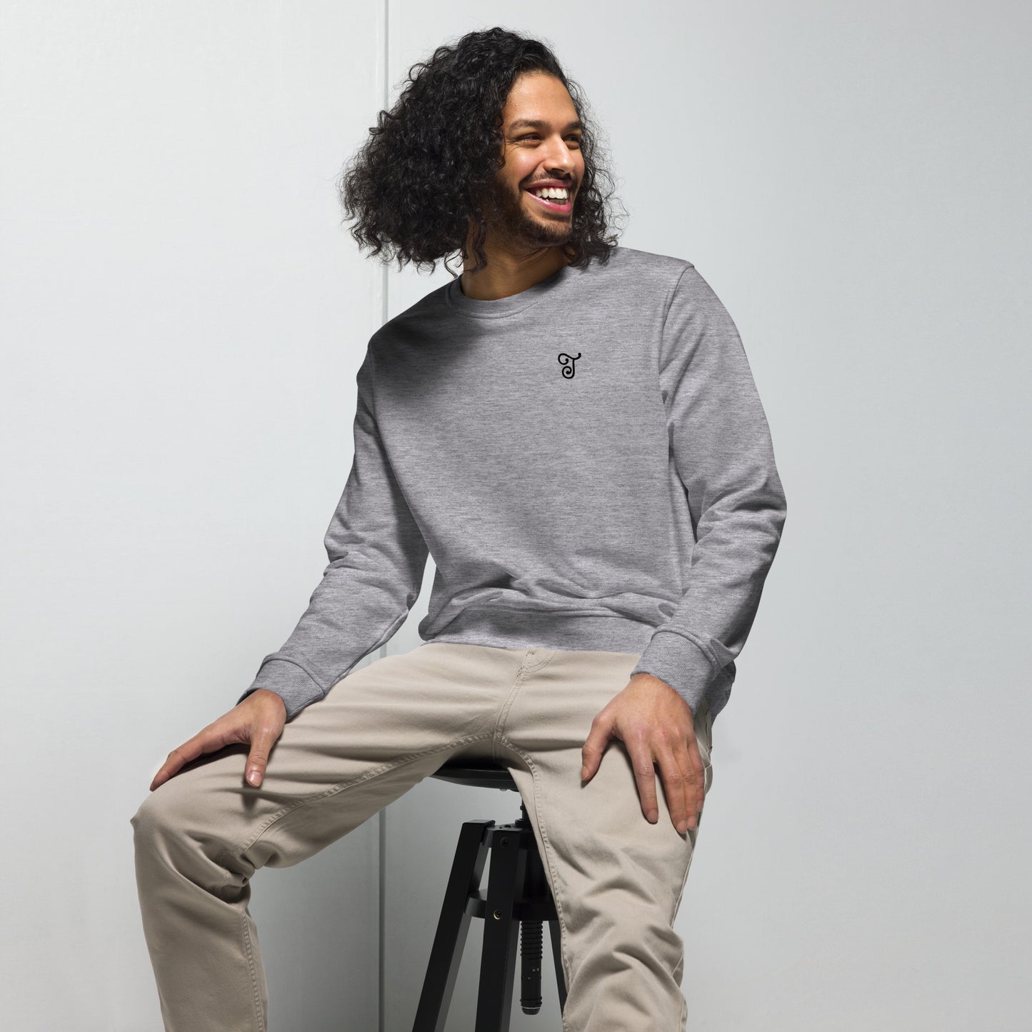 Grey sweatshirt featuring an embroidered letter ‘T’ on the left chest, worn with beige pants, seated on a black stool against a white background—modern, stylish, and available in multiple colors.