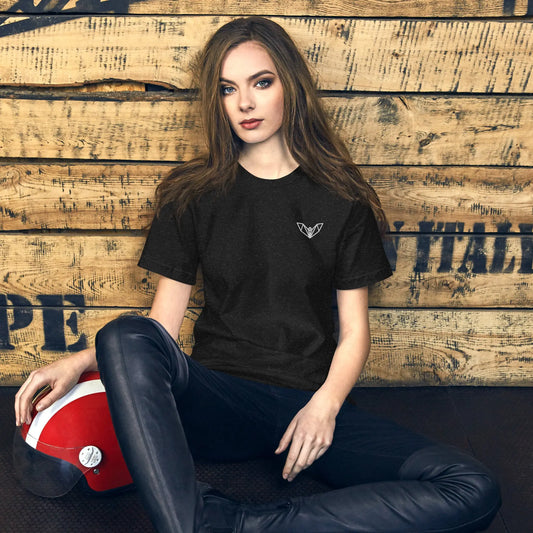 Black women’s t-shirt featuring a small white geometric bat logo on the left side of the chest, worn while seated on a wooden floor with a red and white helmet nearby—sleek, minimalist, and perfect for casual and athletic wear.