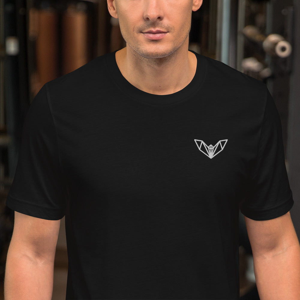 Black athletic t-shirt featuring a sharp geometric bat logo in white on the left side of the chest, worn in a gym environment with various exercise equipment—sleek, edgy, and perfect for fitness and casual wear.
