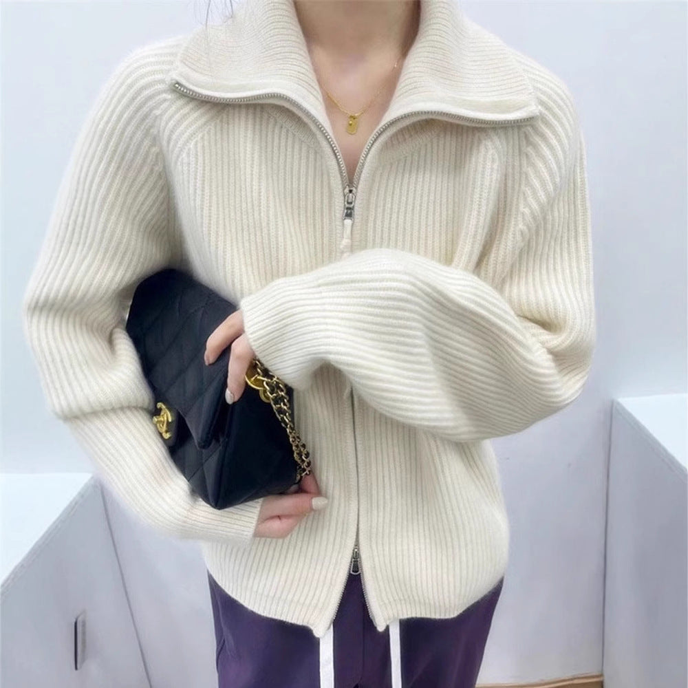 Woman wearing a white ribbed knit sweater with a high collar and a partially zipped front, styled with light pink pants and delicate accessories—cozy, stylish, and perfect for layering.