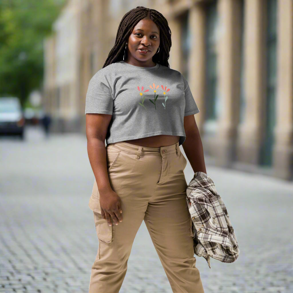 White crop top featuring a delicate printed floral design of three flowers in pink, orange, and yellow with green stems, worn with beige cargo pants and holding a plaid shirt—modern, stylish, and available in multiple colors.