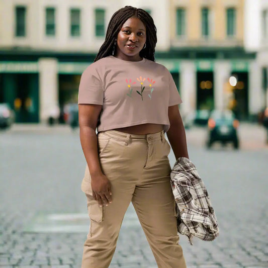 White crop top featuring a delicate printed floral design of three flowers in pink, orange, and yellow with green stems, worn with beige cargo pants and holding a plaid shirt—modern, stylish, and available in multiple colors.