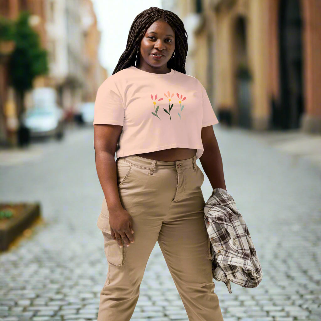 White crop top featuring a delicate printed floral design of three flowers in pink, orange, and yellow with green stems, worn with beige cargo pants and holding a plaid shirt—modern, stylish, and available in multiple colors.
