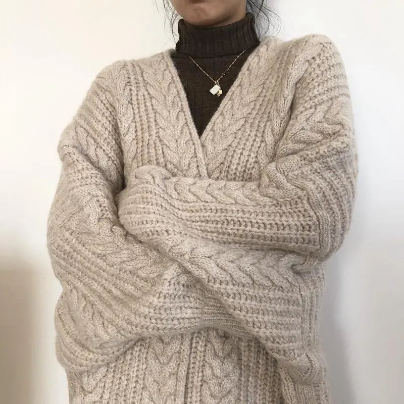 Person wearing a beige cable knit sweater against a plain background