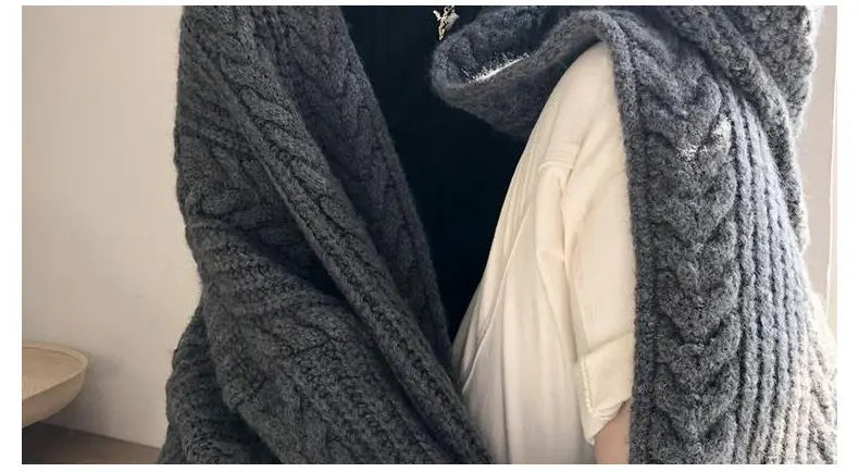 Close-up of a person wearing a chunky knit hooded cardigan in dark gray, layered over a cream shirt and black top. The image includes a text overlay at the bottom describing the single-row open-knit design.