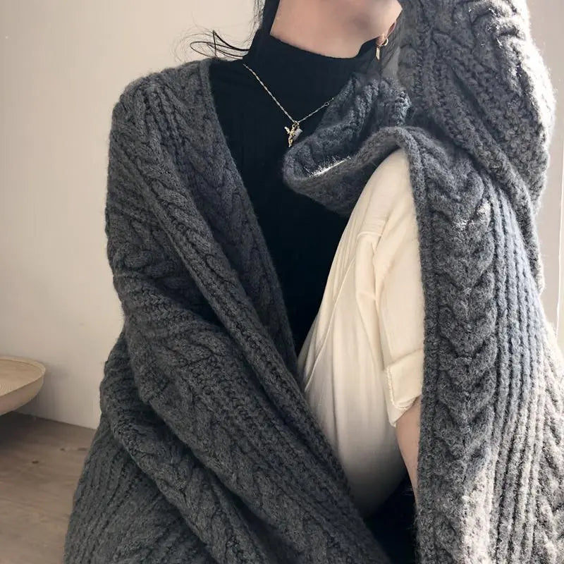 Person wearing a gray knitted cardigan with a plain background