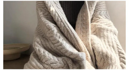 Close-up of a chunky cable-knit sweater in a warm cream or oatmeal beige color, draped on a person. The image includes a text overlay at the bottom describing the waist detailing.