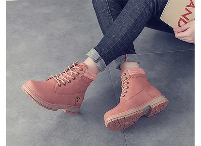 A pair of pink lace-up ankle boots worn with dark blue jeans, shown in two views on a gray tiled floor. The top view shows the boots from a side angle while the person sits, and the bottom view shows them from a top-down angle with a small card on the floor.