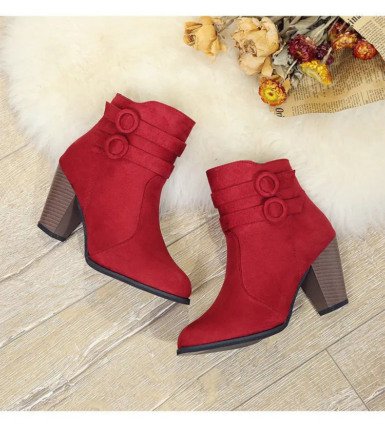 A pair of red suede ankle boots with chunky brown block heels and decorative side buttons, displayed on a light wood floor over a white faux fur rug with dried flowers. A white banner at the bottom reads 'TODAY NEW ARRIVAL'.