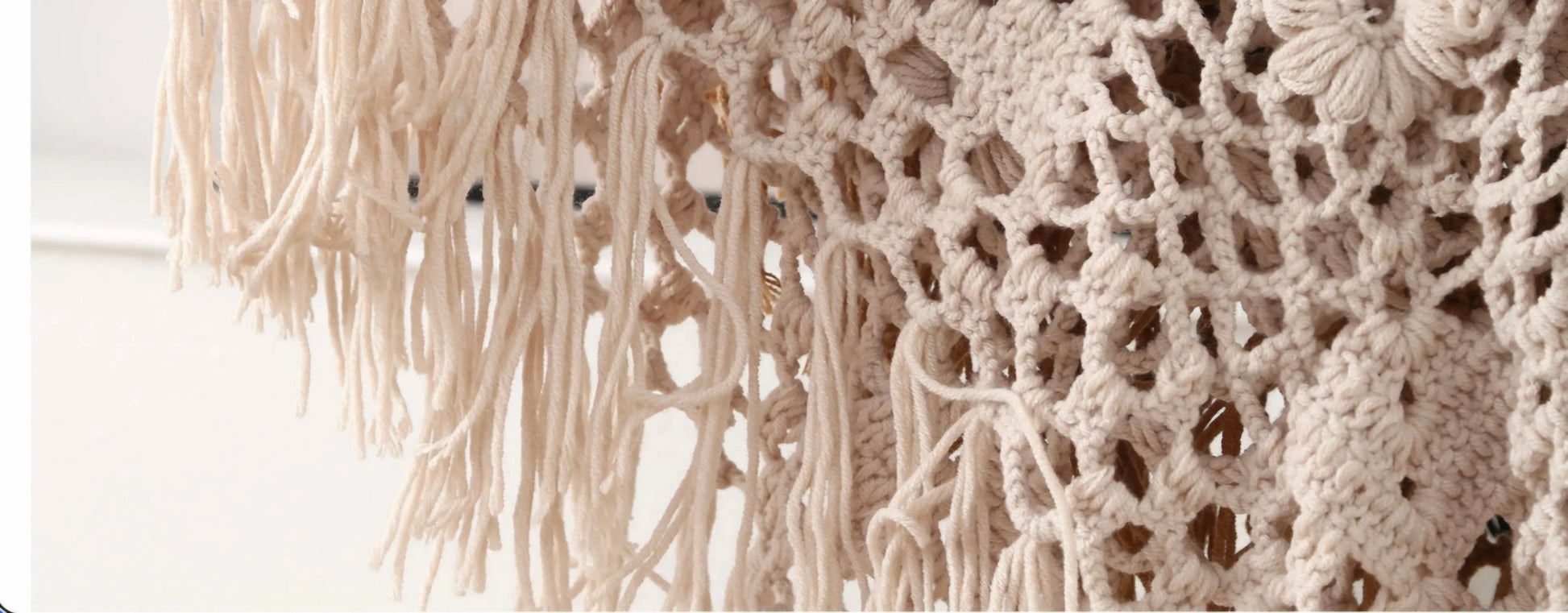Close-up of a cream-colored crocheted or knitted textile with long fringe and openwork floral-like patterns.