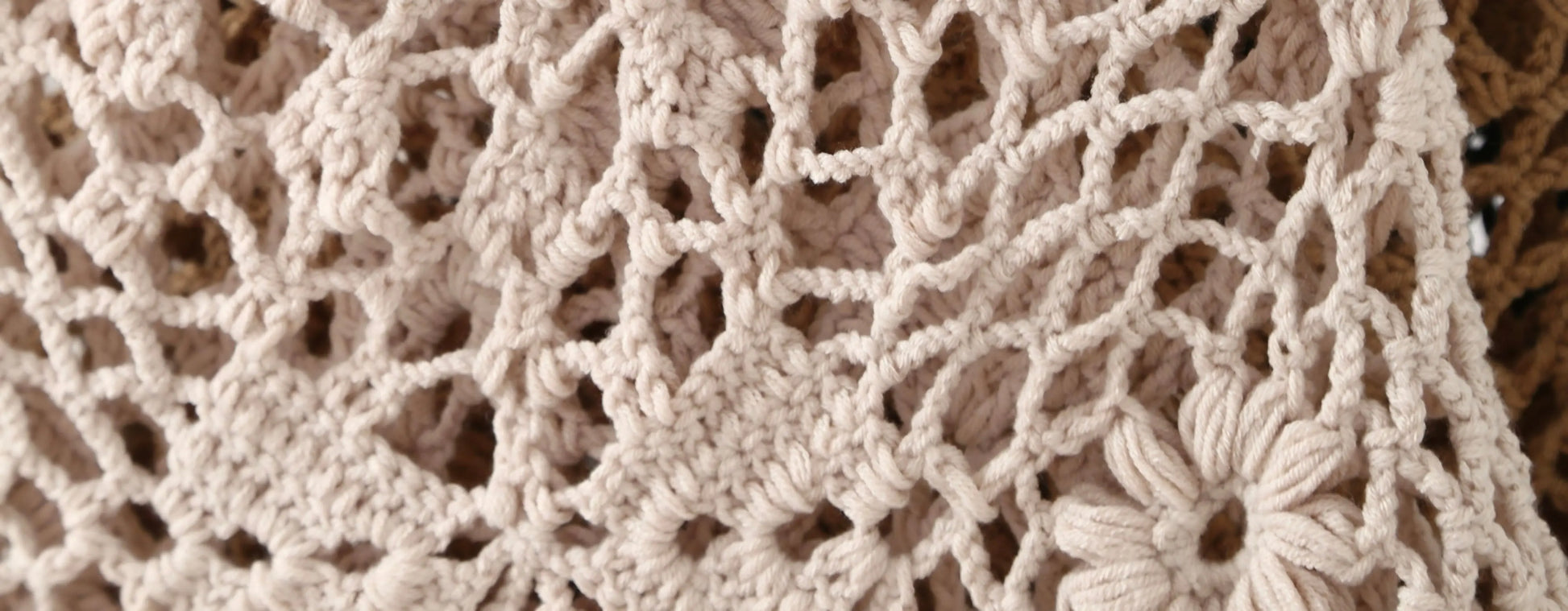 Close-up of a beige crochet or lace textile with an openwork floral pattern, showing the texture and stitch detail.