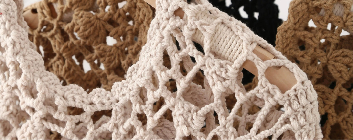 Close-up of a chunky crocheted or knit mesh garment in a light beige/cream tone, with brown and black versions partially visible in the background.