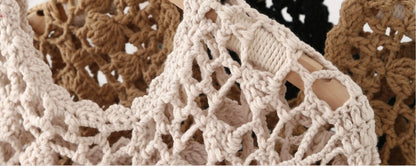 Close-up of a chunky crocheted or knit mesh garment in a light beige/cream tone, with brown and black versions partially visible in the background.