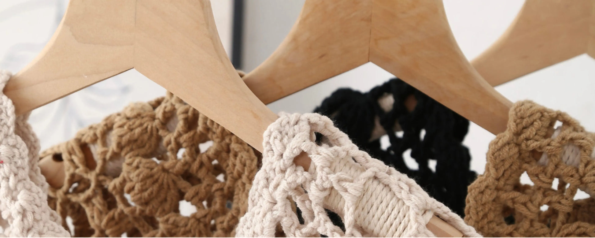 Close-up of crocheted or lace-trimmed tops hanging on wooden hangers, showing beige, brown, and black fabric details against a light background.