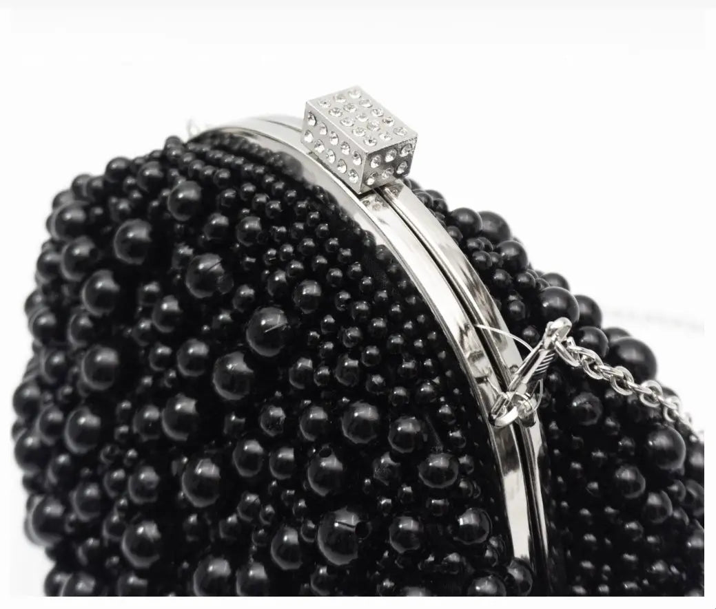 A close-up of a black beaded clutch purse with a silver-tone metal frame and a rhinestone-embellished clasp, set against a plain white background.