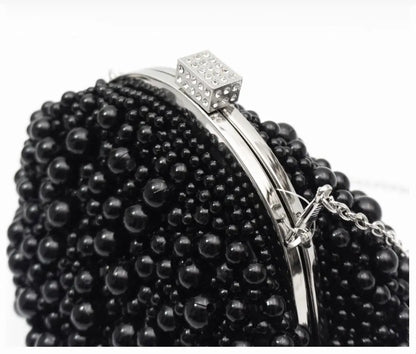 A close-up of a black beaded clutch purse with a silver-tone metal frame and a rhinestone-embellished clasp, set against a plain white background.