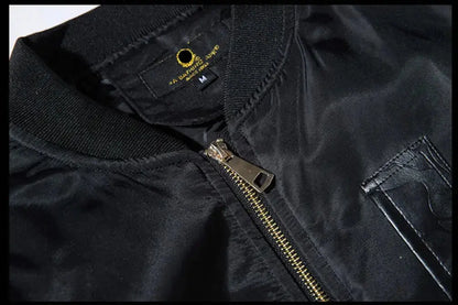 Close-up of a black nylon bomber jacket showing the ribbed collar, a gold-tone zipper, and a black neck label with a gold logo.