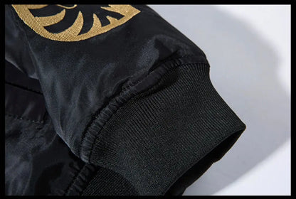 Close-up detail of a black bomber jacket sleeve featuring a ribbed knit cuff and a gold embroidered circular emblem on the upper arm.