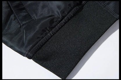 Close-up detail of a black garment showing a textured elasticated cuff and a smooth fabric panel on a white background.
