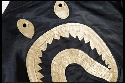 Close-up of a black garment featuring a large beige embroidered or appliqué curved motif with scalloped edges and two small matching beige patches on the upper portion.