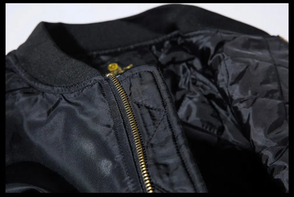 Close-up of a black bomber jacket showing the ribbed collar, gold zipper, and quilted black nylon interior lining.