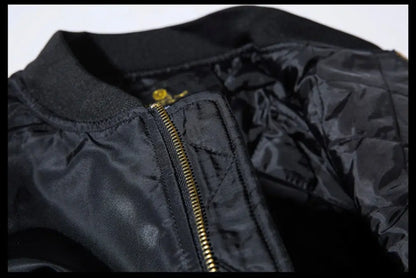 Close-up of a black bomber jacket showing the ribbed collar, gold zipper, and quilted black nylon interior lining.