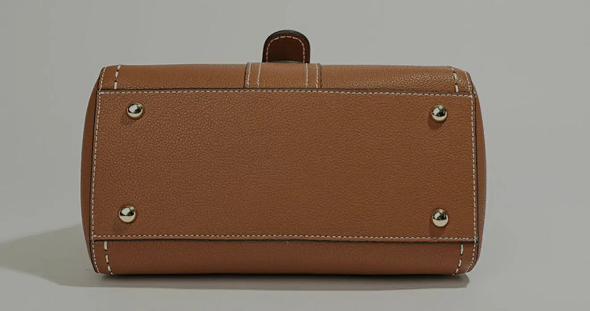 A brown pebbled leather clutch bag with silver-tone metal studs and white contrast stitching, shown from the front on a neutral gray background.