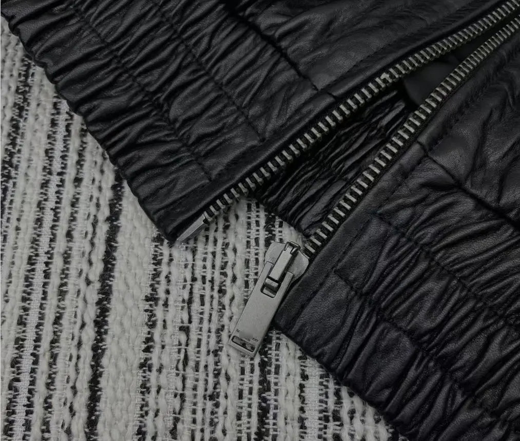 Close-up of a black quilted leather jacket with a silver zipper, laid flat on a black and white textured woven rug.