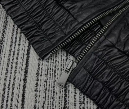 Close-up of a black quilted leather jacket with a silver zipper, laid flat on a black and white textured woven rug.